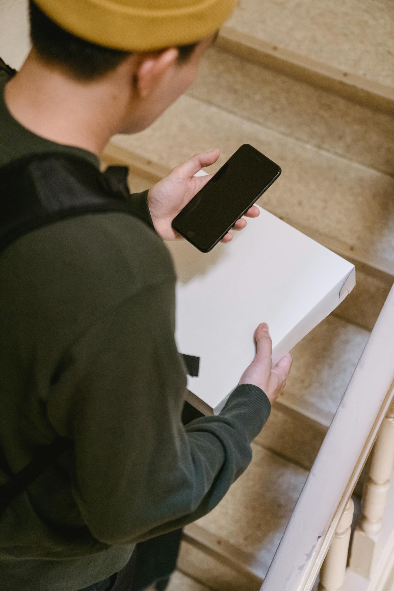A delivery person checking their phone while holding a package on the stairs.